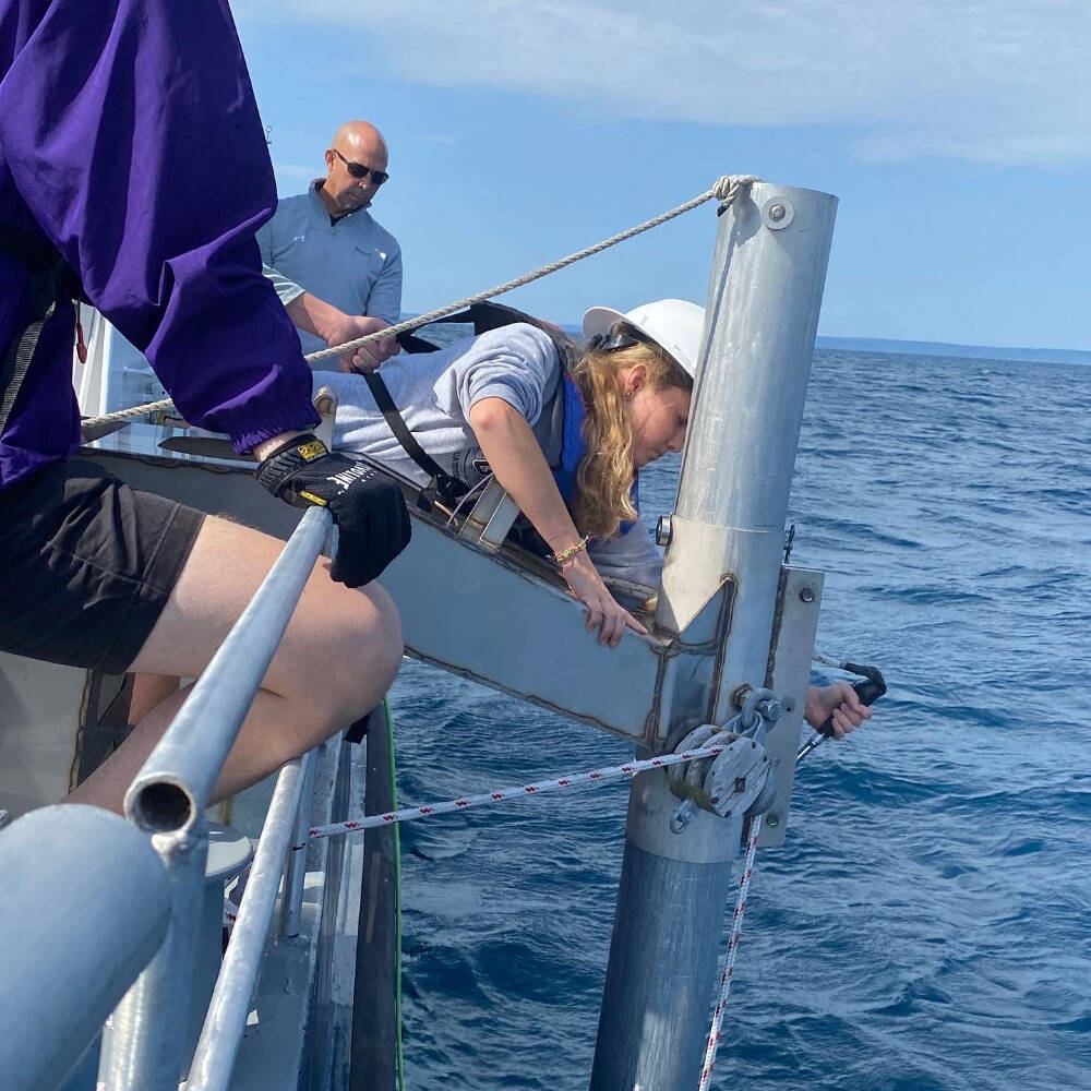 Three people on a boat working with a metallic beam over the ocean.